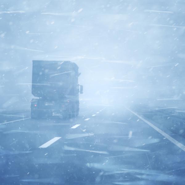 A transport truck on a snow-covered road in a blizzard.