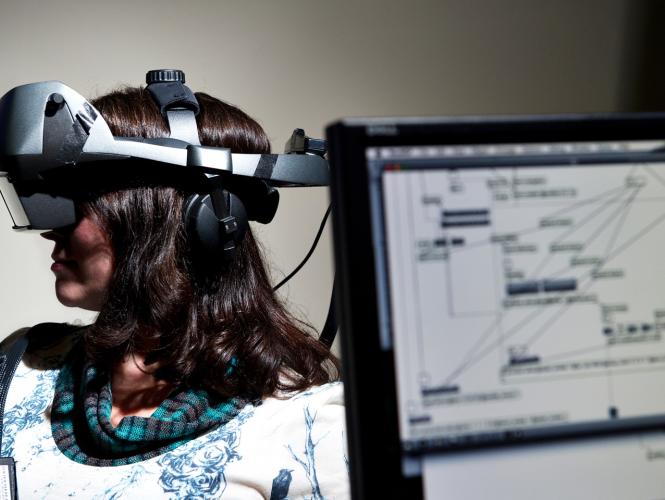 A person wears a headset covering their eyes with computer screen in foreground