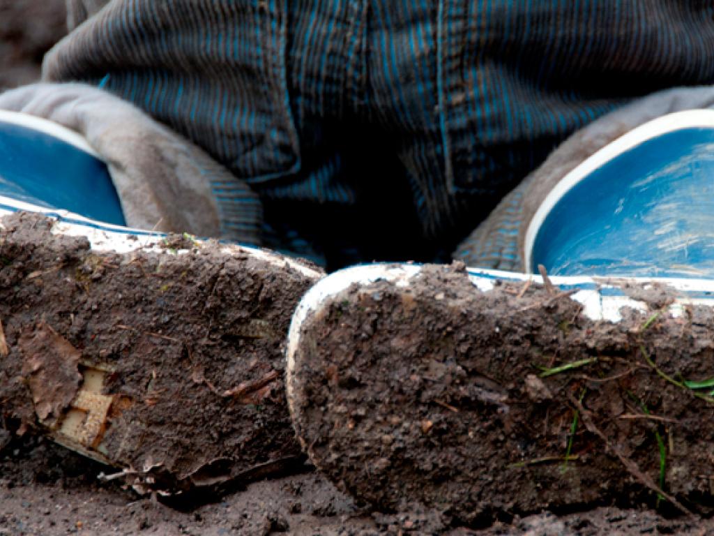 Les semelles des bottes de caoutchouc bleues d’un enfant, imprégnées de boue