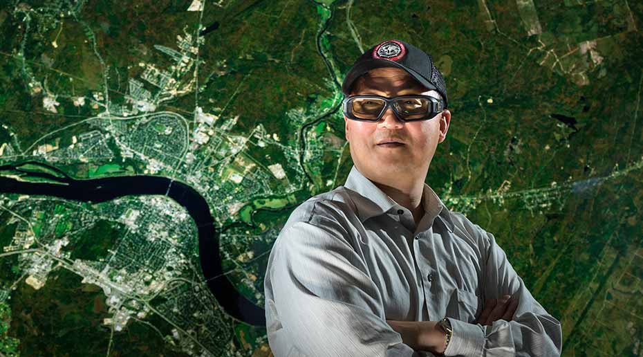 Yun Zhang, de l'Université du Nouveau-Brunswick, pose pour la photo sur une image satellite d'une zone métropolitaine.