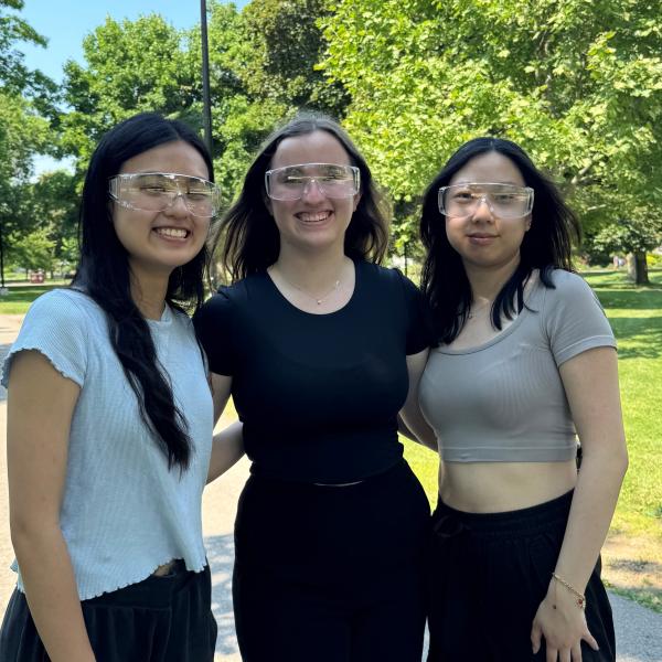 Trois jeunes femmes portant des lunettes de sécurité en plastique transparent, posent pour la photo à l’extérieur