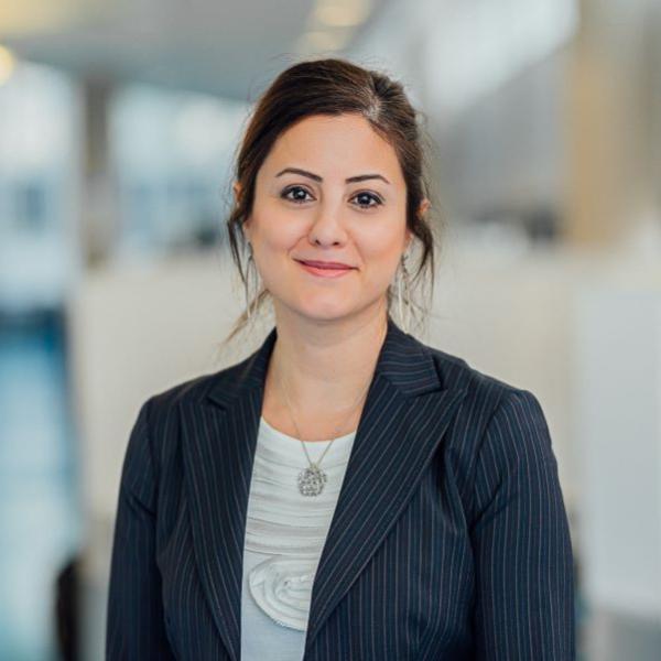 Portrait of a person wearing large earrings and a dark blue jacket with pale blue, rose and burgundy stripes.