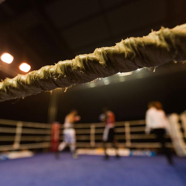 Looking through the ropes into a boxing ring, with boxers blurred in the background.