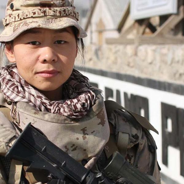 Une femme vêtue d’un uniforme militaire regarde la camera, pointe un arme vers le sol.