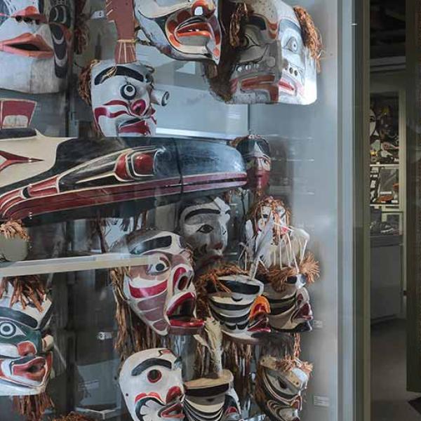 A dimly-lit museum room has several display cases with colourfully painted indigenous masks.