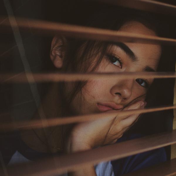 Une jeune femme regarde par la fenêtre à travers les volets ouverts, l’air ennuyé