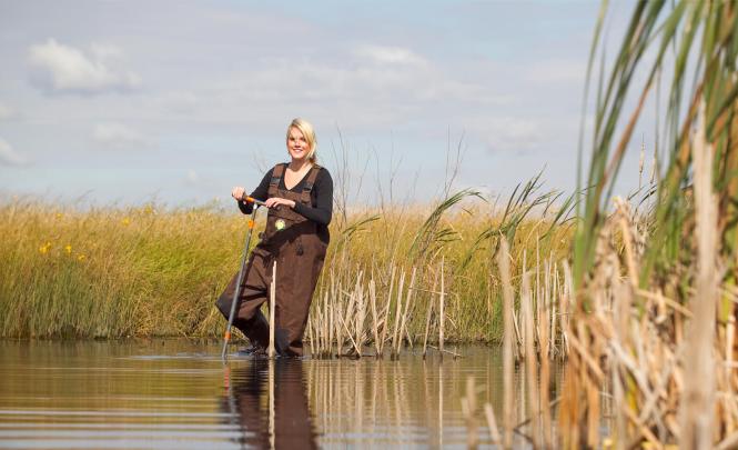 Une personne posant pour la photo les pieds dans de l'eau marécageuse peu profonde.