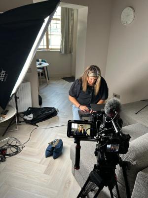 Hilary Earl kneels on the floor with her laptop as she prepares for an interview. In the foreground is a video camera.