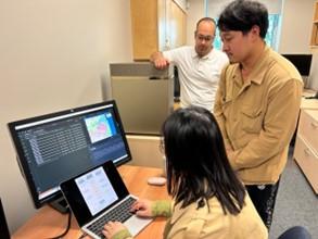 Three team members grouped around a laptop computer and a very large monitor displaying a map of Hamilton, Ontario, while one member leans on an AI server. 