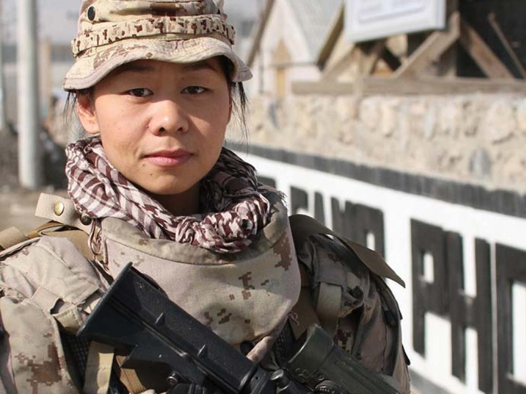 Une femme vêtue d’un uniforme militaire regarde la camera, pointe un arme vers le sol.