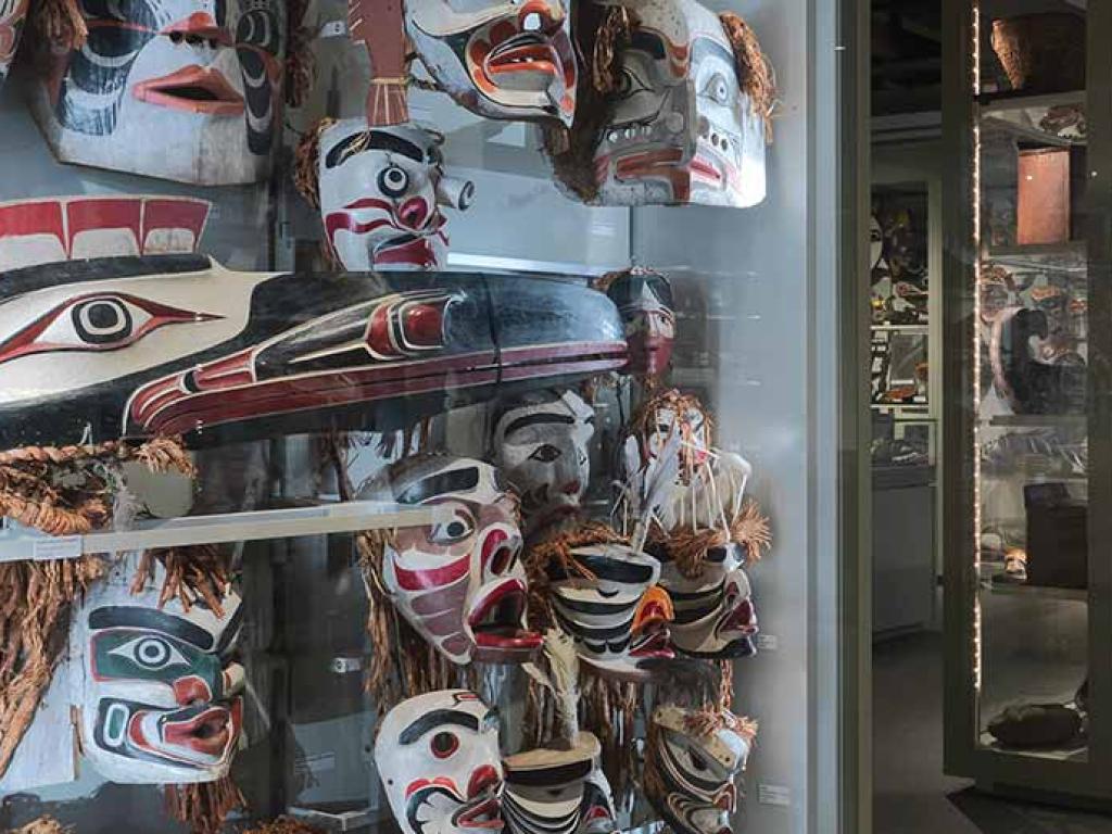 Une salle de musée peu éclairée compte de nombreux présentoirs affichant des masques autochtones peints de couleurs vives.