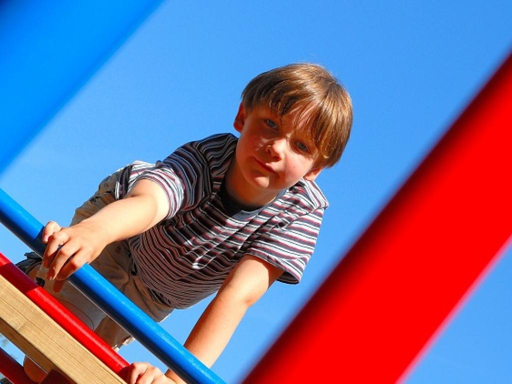Un jeune garçon regarde à travers les barres d’un module de jeux